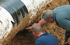 Two men examining a [pipeline after excavation